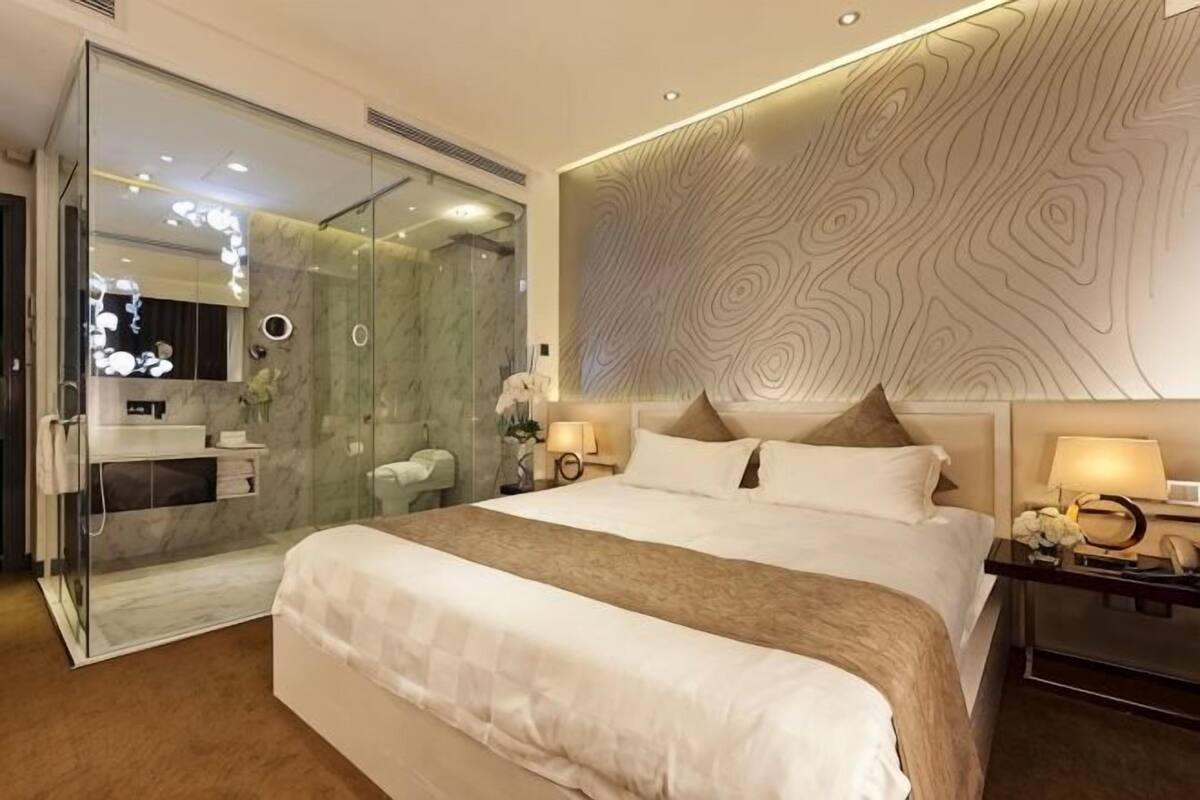Habitación de hotel moderna con una cama grande, ducha con cerramiento de vidrio, pared de mármol y un diseño de pared con textura única.