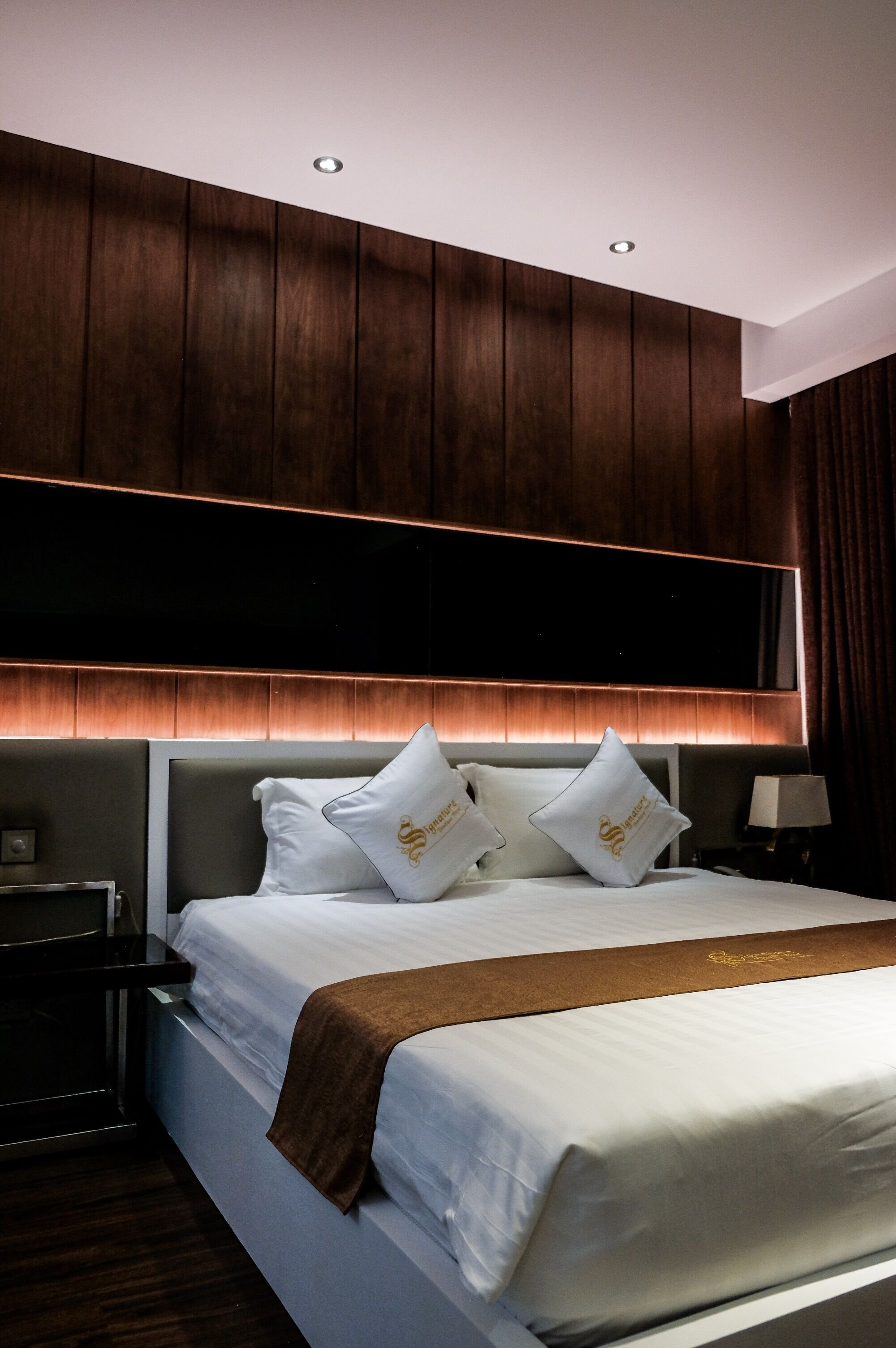A hotel room with a large bed, wooden panel headboard, white bedding, and a brown throw blanket.