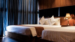Une chambre d’hôtel avec deux lits, des boiseries, une grande fenêtre avec des rideaux et une table de chevet avec une lampe.