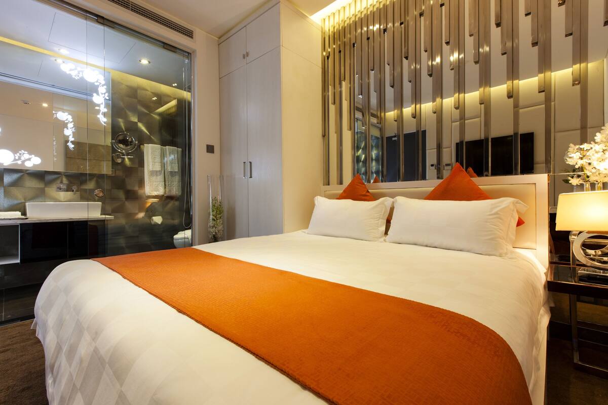 Una habitación de hotel moderna con una cama grande, cabina de ducha de vidrio y un diseño de pared contemporáneo.