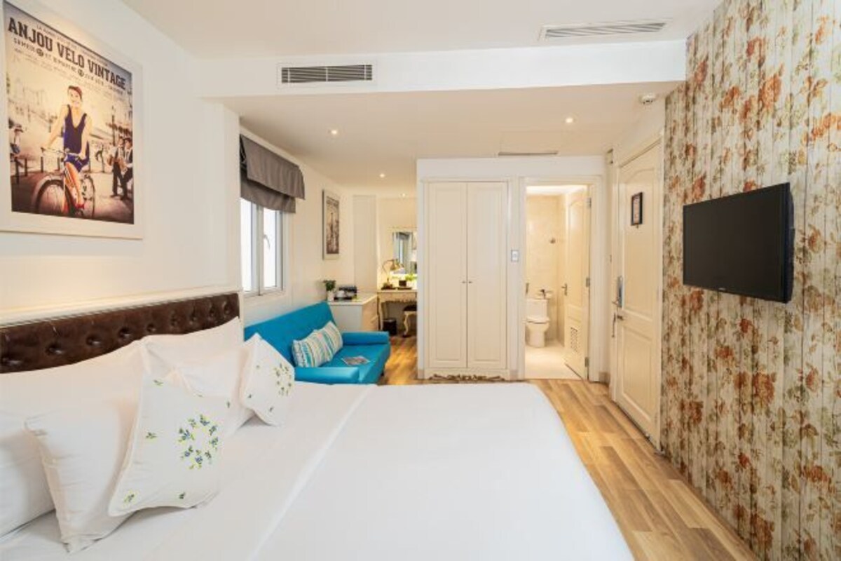 A hotel room with a bed, a blue sofa, a television, and a bathroom visible through an open door.