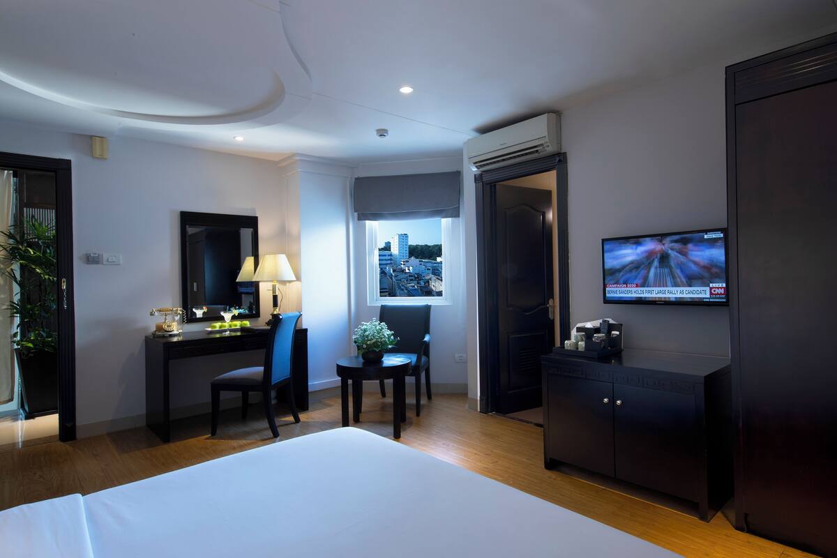 Een hotelkamer met een bed, bureau, stoel, televisie en uitzicht op de stad door het raam.