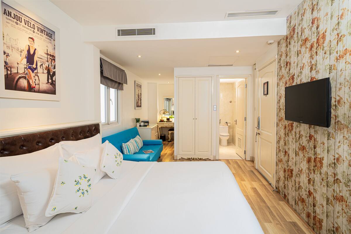 Een slaapkamer met een groot bed, een blauwe bank, een televisie en een badkamer door een open deur zichtbaar.