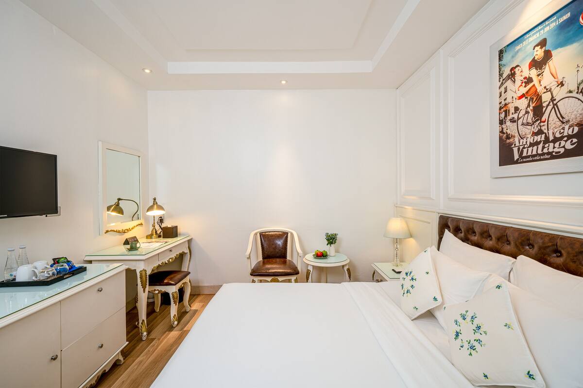 Een hotelkamer met een bed, een bureau met stoel, een televisie en een poster aan de muur.