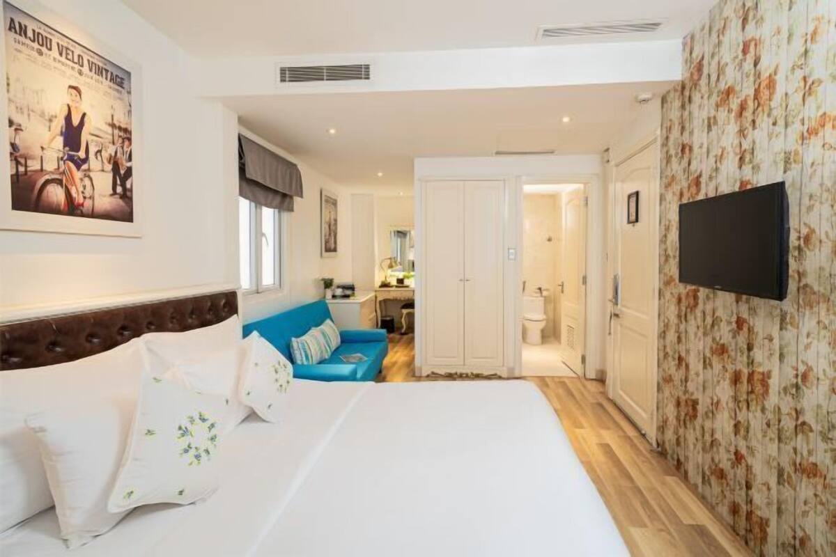 Een hotelkamer met een bed, een blauwe bank, een televisie en een badkamer die door een open deur zichtbaar is.