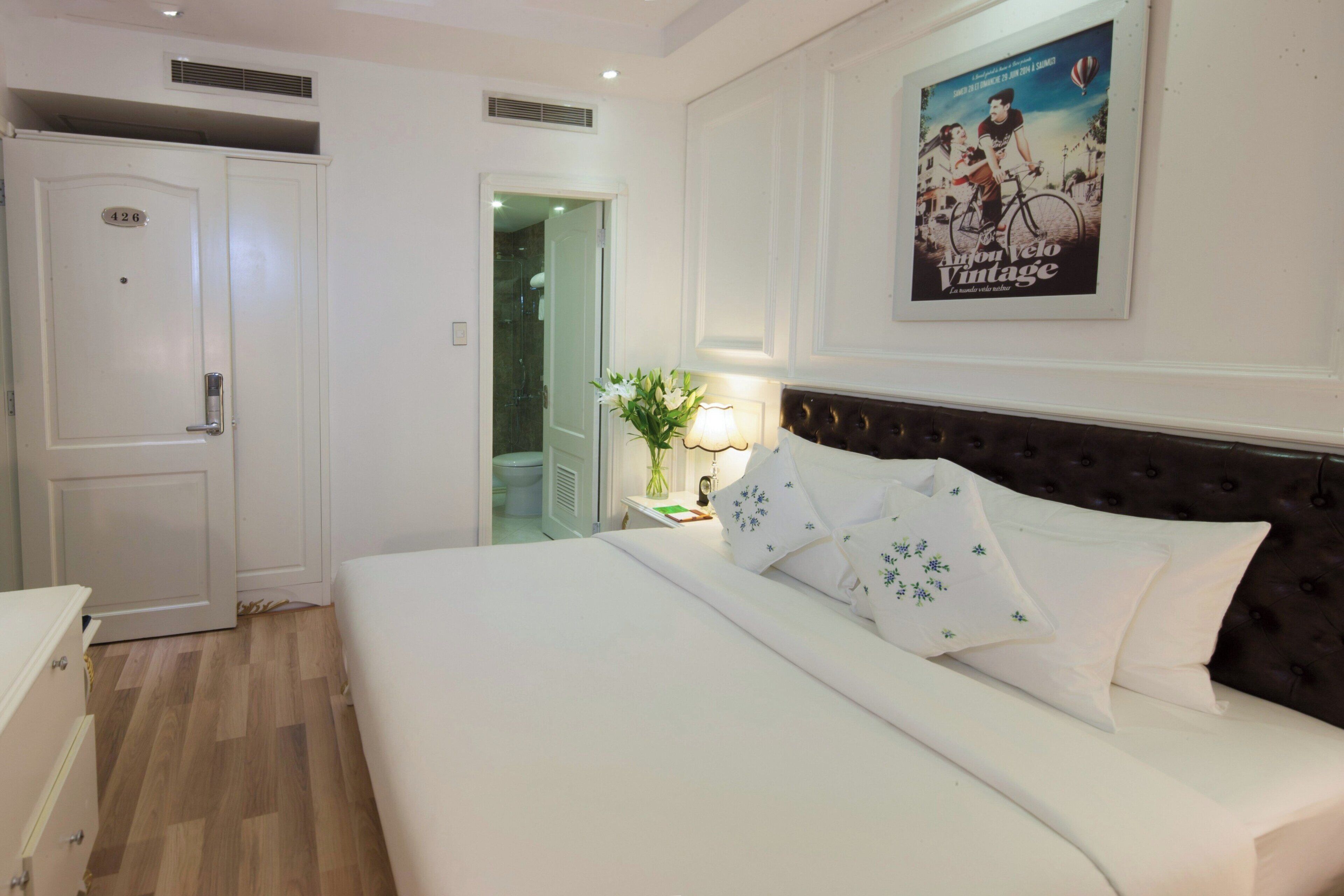 Ein Hotelzimmer mit einem Bett, einem Nachttisch, einer Lampe und einem Poster an der Wand.