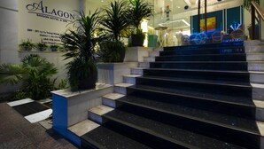 L’entrée d’un hôtel, avec un escalier menant au hall d’accueil, des plantes en pot et une enseigne indiquant « Alagon Saigon Hotel & Spa ».