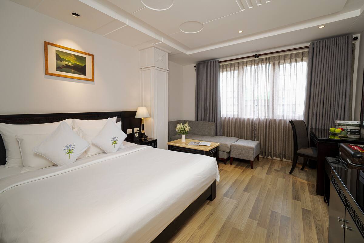 Een hotelkamer met een groot bed, een bureau met stoel, een bijzettafeltje met lamp en een raam met gordijnen.