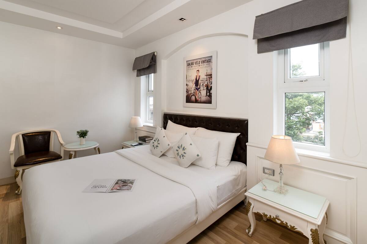 Een netjes ingerichte hotelkamer met een groot bed, een klein nachtkastje met een lamp, een stoel en een poster aan de muur.