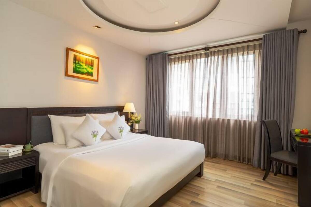 Een hotelkamer met een groot bed, een nachtkastje, een lamp, een stoel en een raam met gordijnen.
