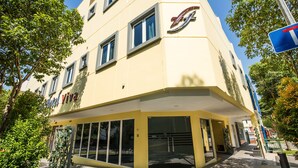 A yellow building with a large glass entrance, a logo on the facade, and a blue sign on the right.
