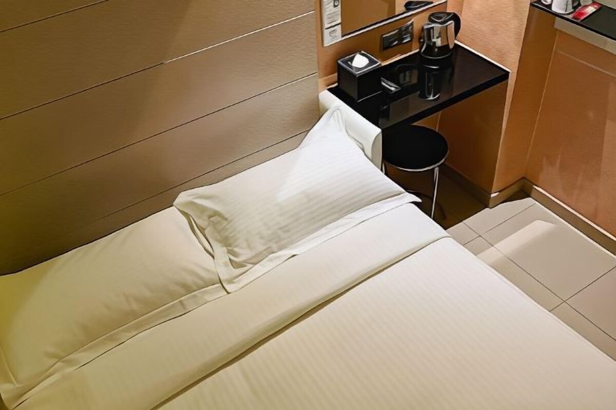 A single bed with white linens in a hotel room.