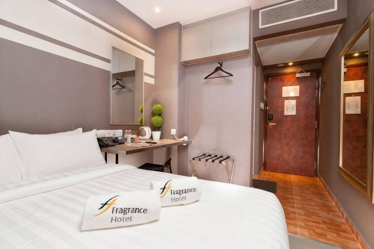 Hotellihuone, jossa on sänky, työpöytä, peili, pieni kasvi ja ovi, joka johtaa kylpyhuoneeseen.