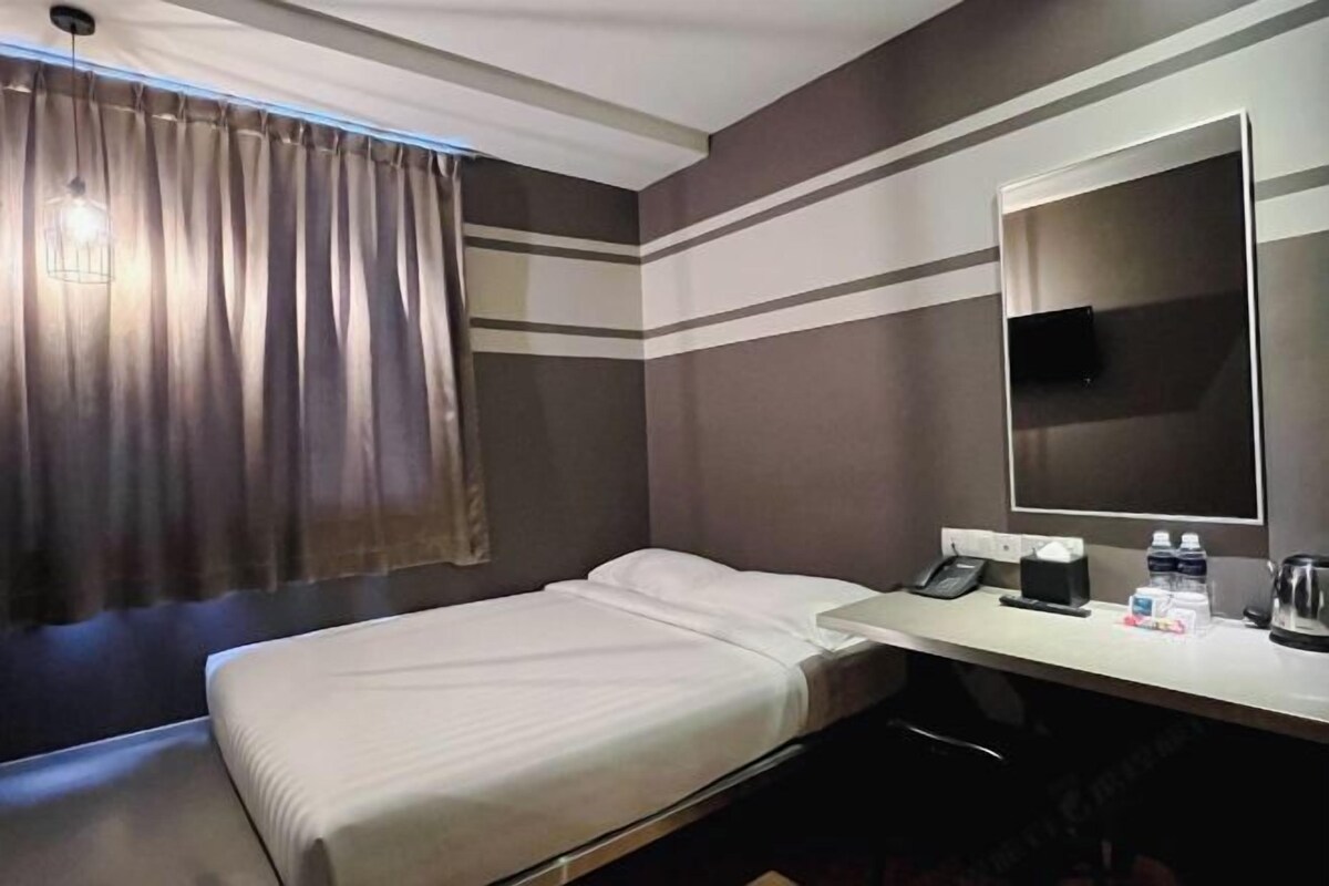 Habitación de hotel con cama, escritorio, teléfono, espejo y ventana con cortinas.