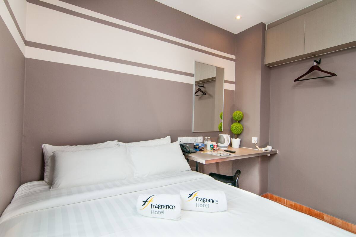 Hotellihuone, jossa on sänky, yöpöytä, peili ja pieni työpöytä tuolilla.