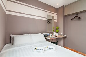 A hotel room with a bed, bedside table, mirror, and a small desk with a chair.