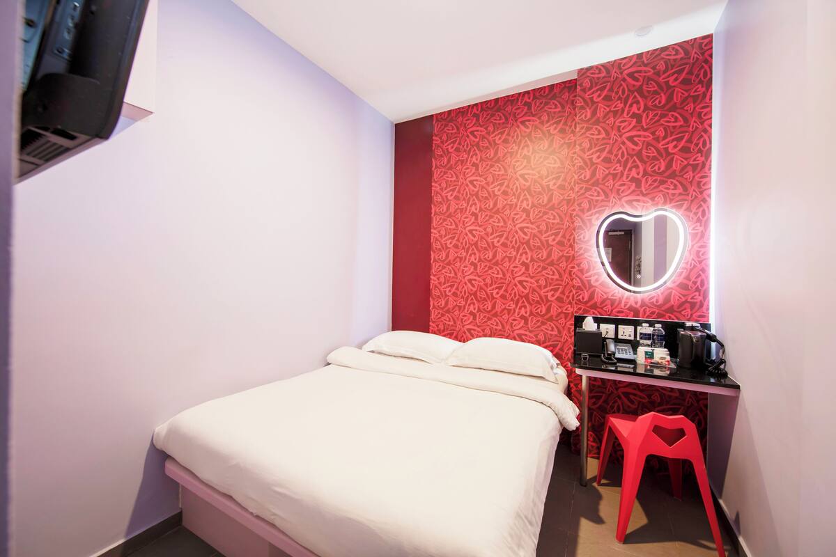 A bedroom with a bed, a desk with a mirror, and a red chair.