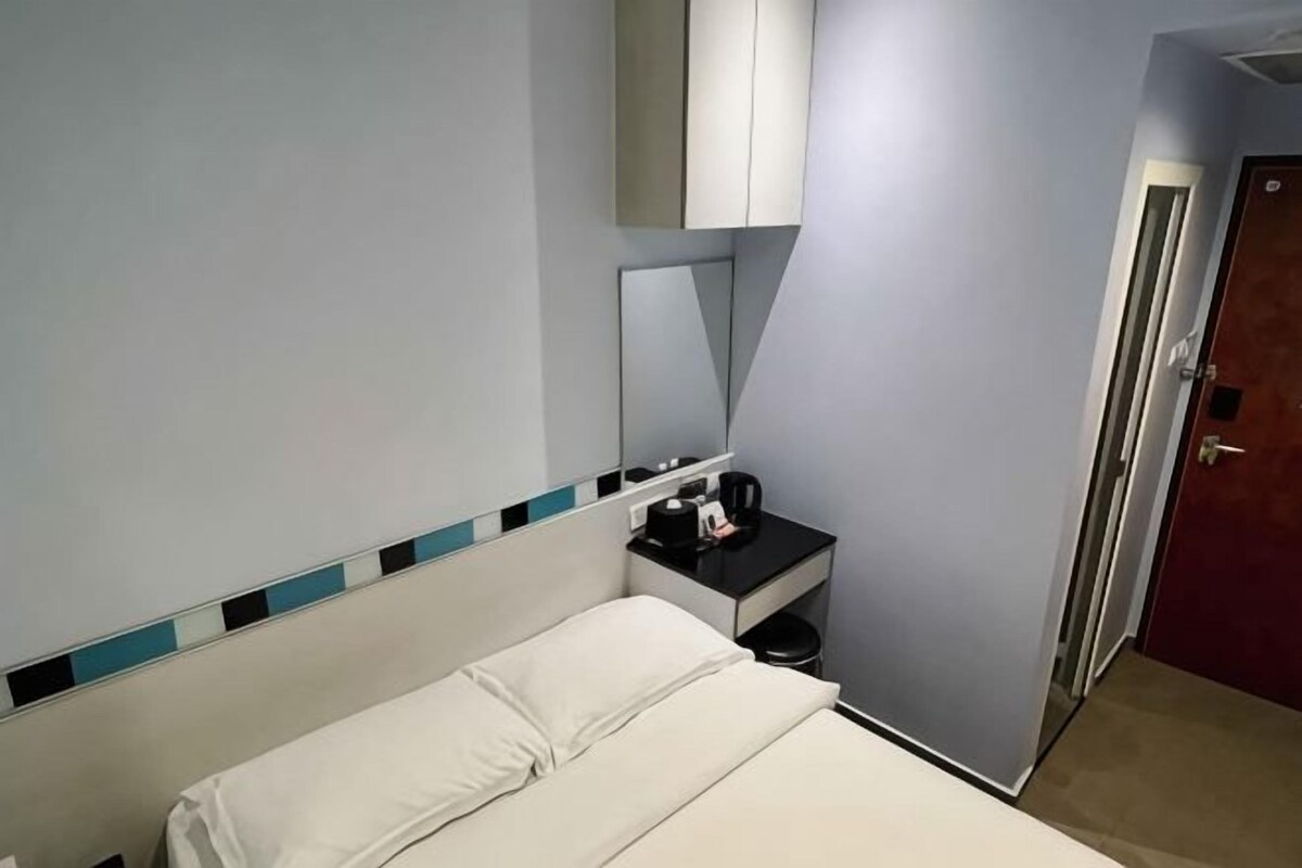 Ein Hotelzimmer mit Bett, Nachttisch, Spiegel, Tür und einem an der Wand befestigten Schrank.