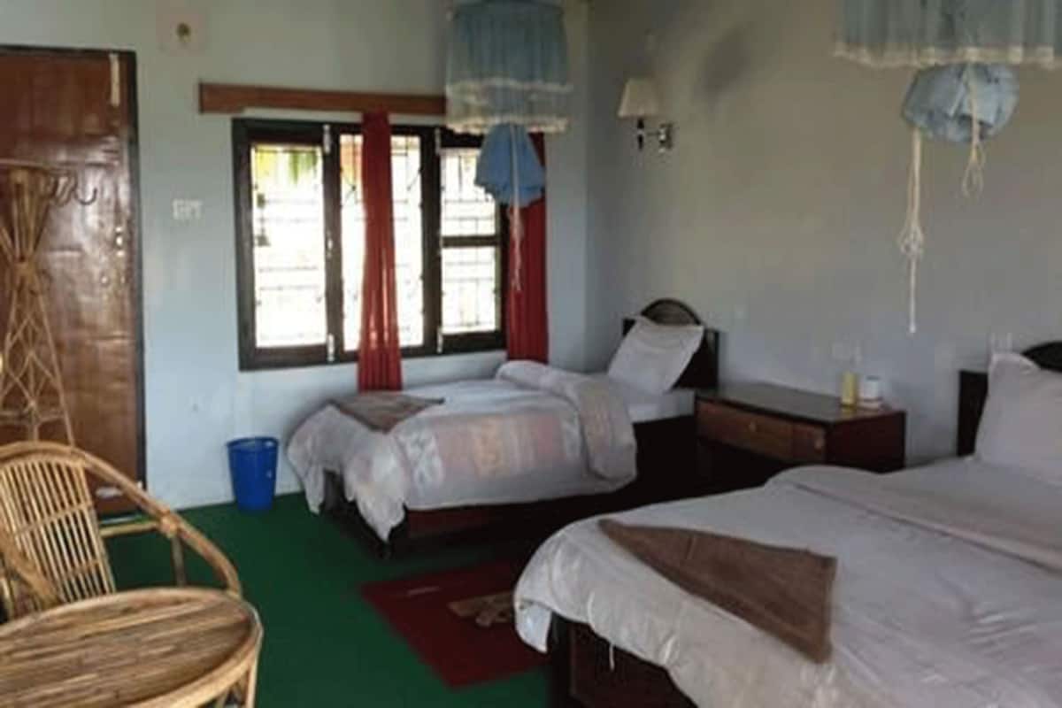 A room with two beds, a wooden chair, a desk, and a window with curtains.