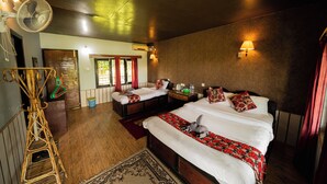 A hotel room with two beds, a large fan, a wooden floor, and a view of the outside. - Wildlife Adventure Resort (Sauraha)