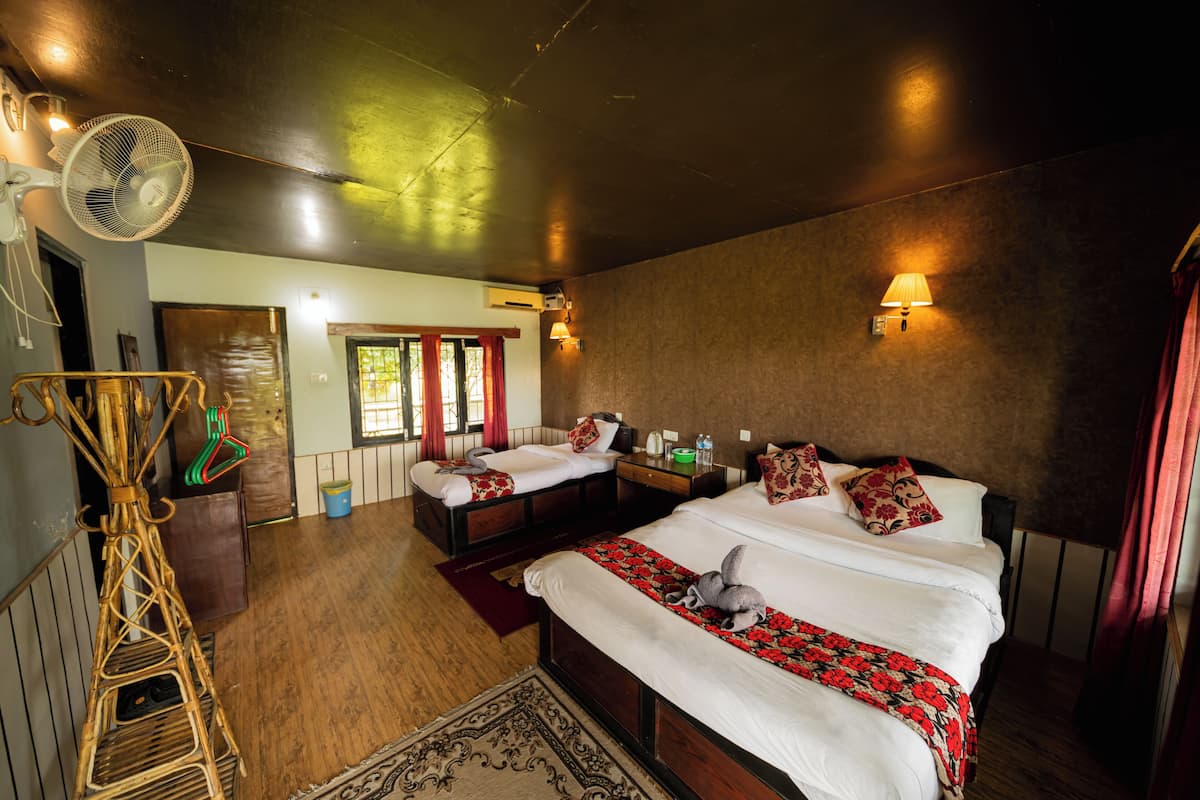 A hotel room with two beds, a large fan, a wooden floor, and a view of the outside.