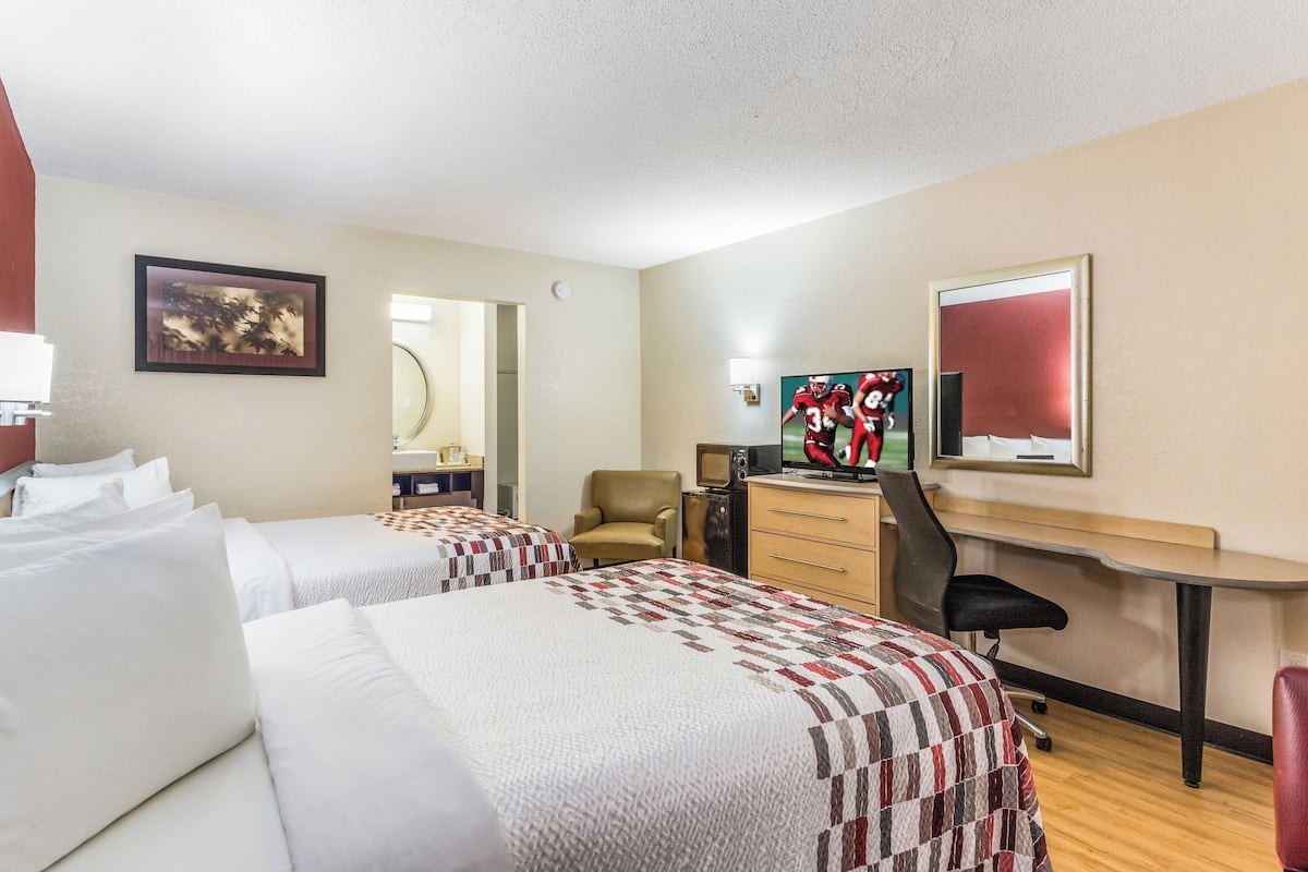 A hotel room with two beds, a desk, a chair, a TV, and a mirror.