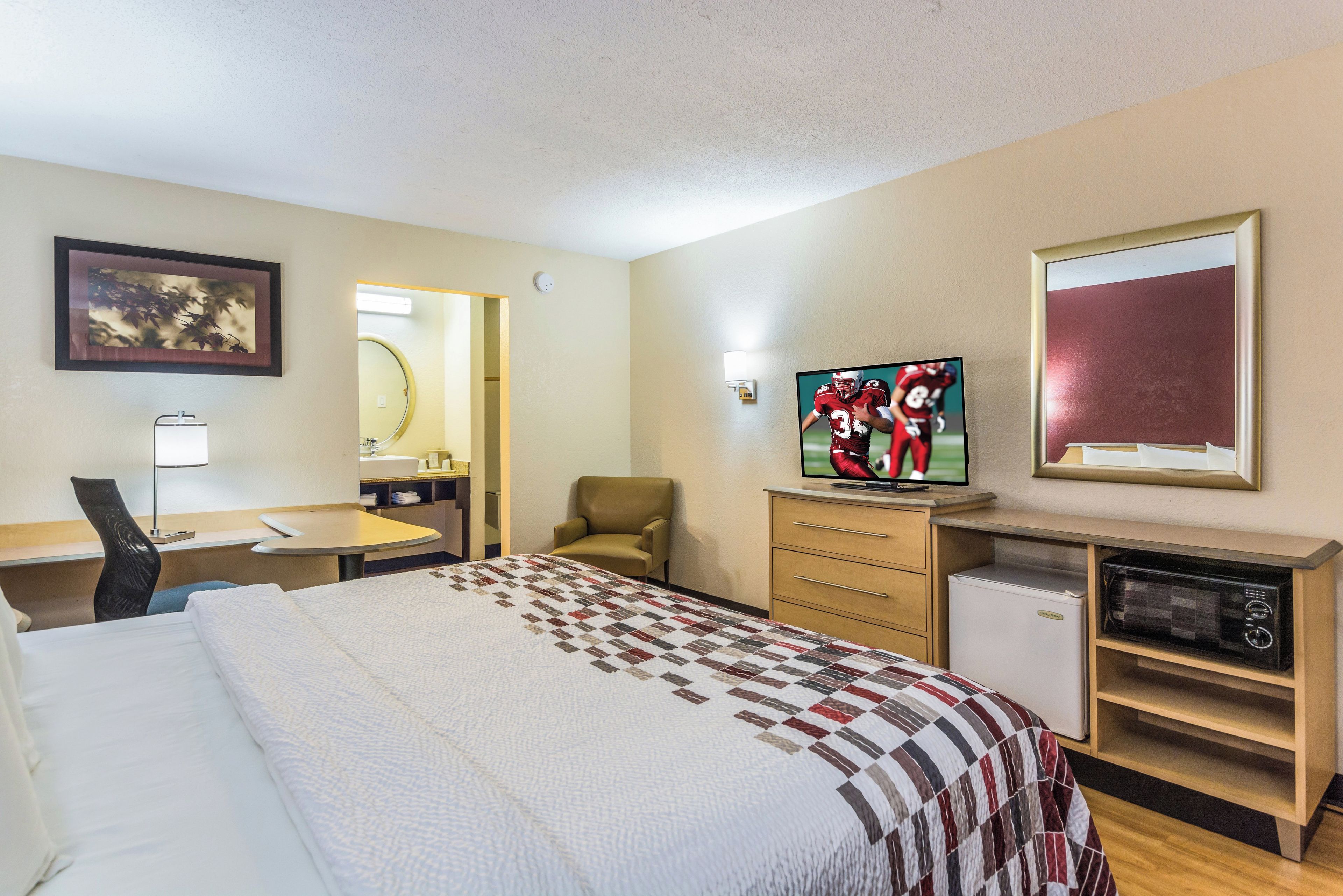 A hotel room with a bed, a desk, a chair, a television, and a microwave.