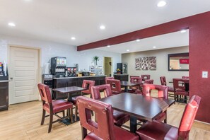 A dining area with tables and chairs, a kitchen area with appliances, and a door. - Red Roof Inn Williamsburg (Williamsburg)