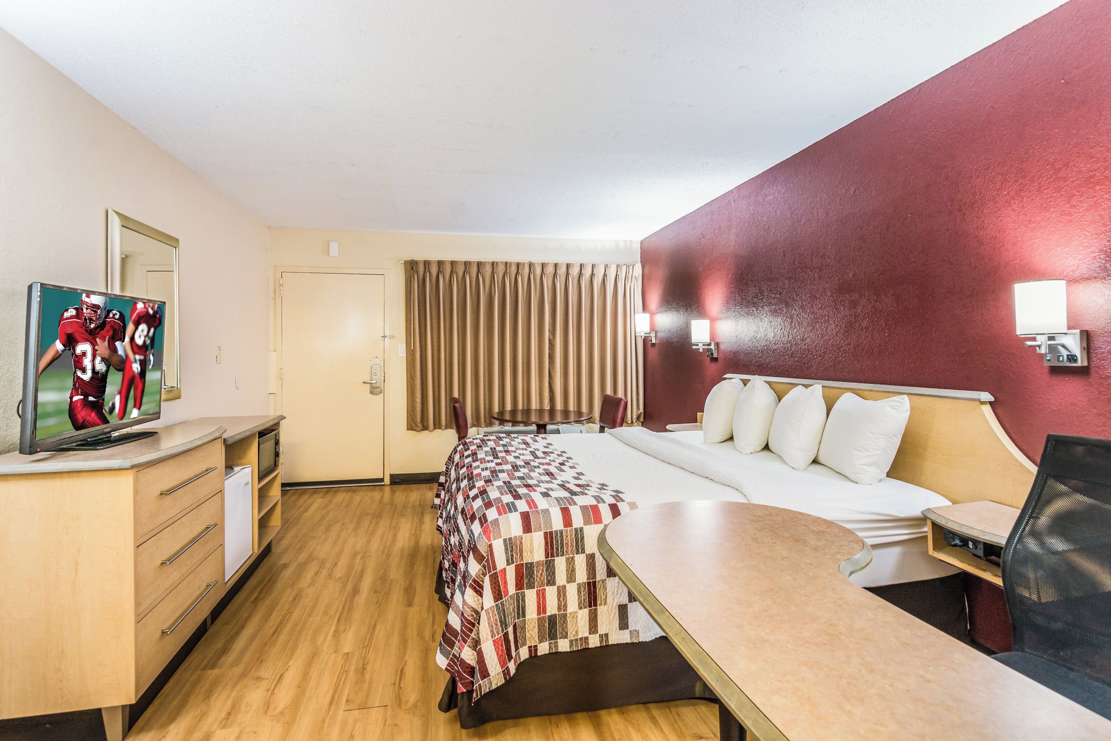 A hotel room with a bed, a desk, a television, a mirror, and a window with curtains.