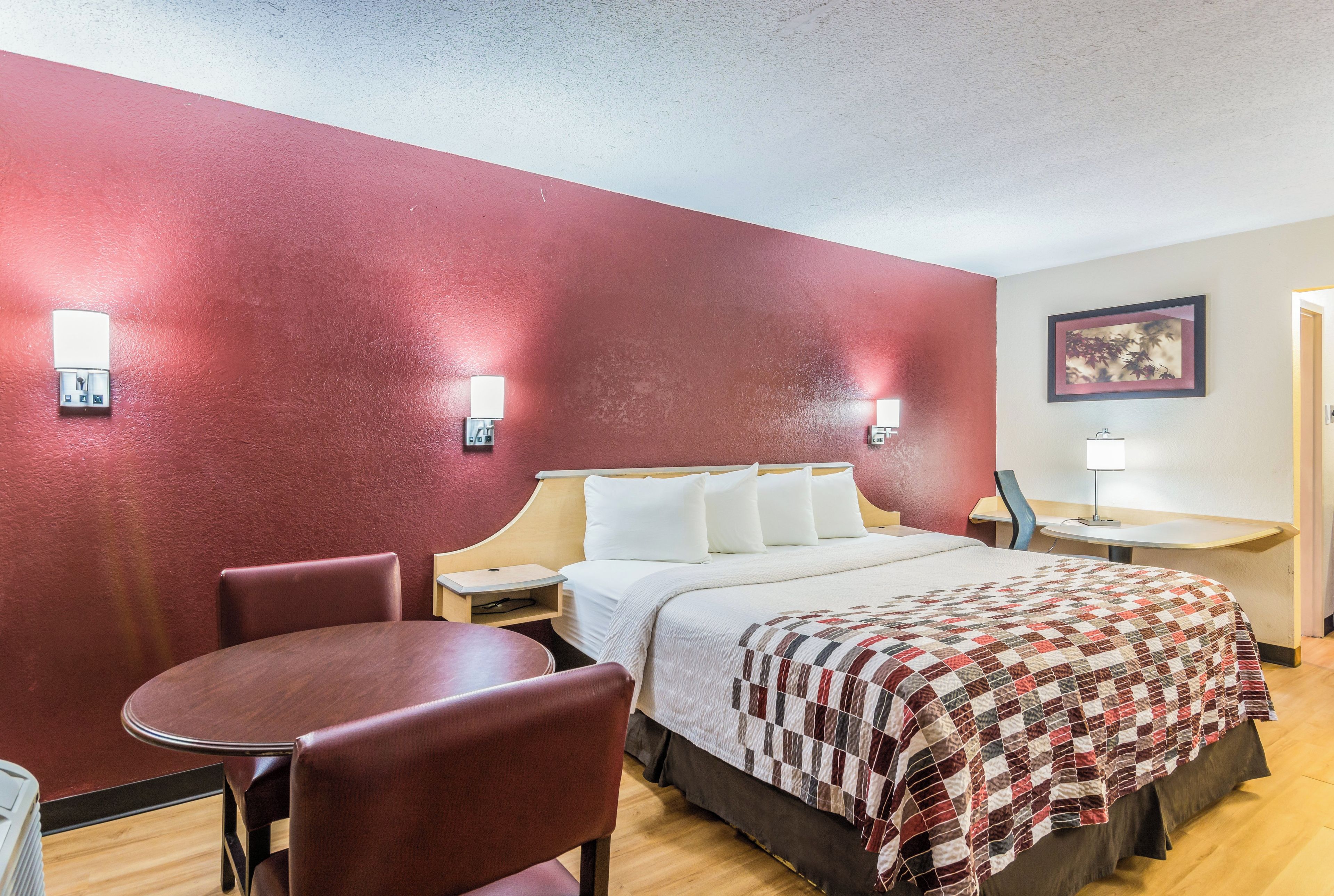 Quarto de hotel com cama, escrivaninha, cadeira e mesa de cabeceira.