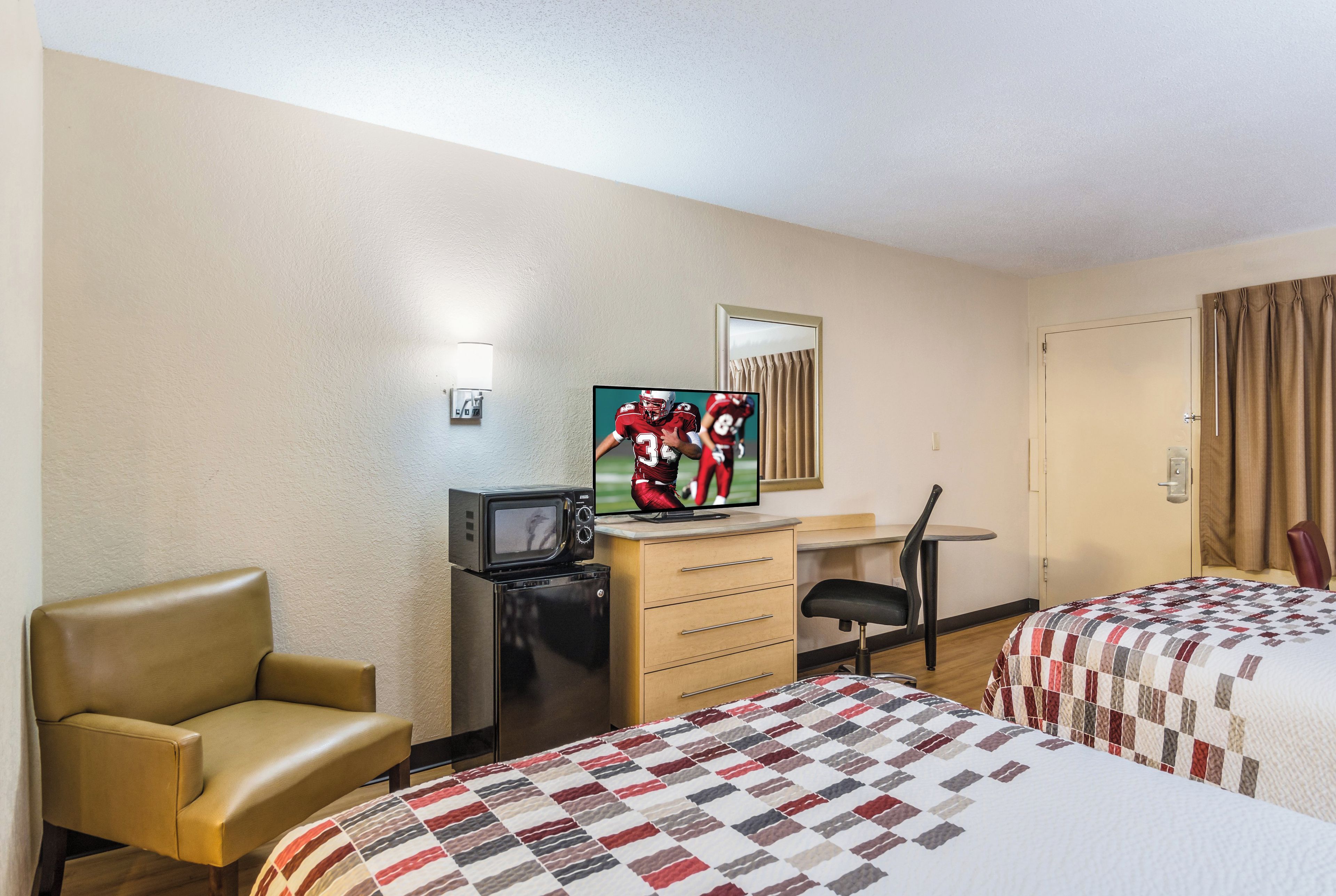 Una habitación de hotel con dos camas, un escritorio, un televisor, una silla y un refrigerador pequeño.