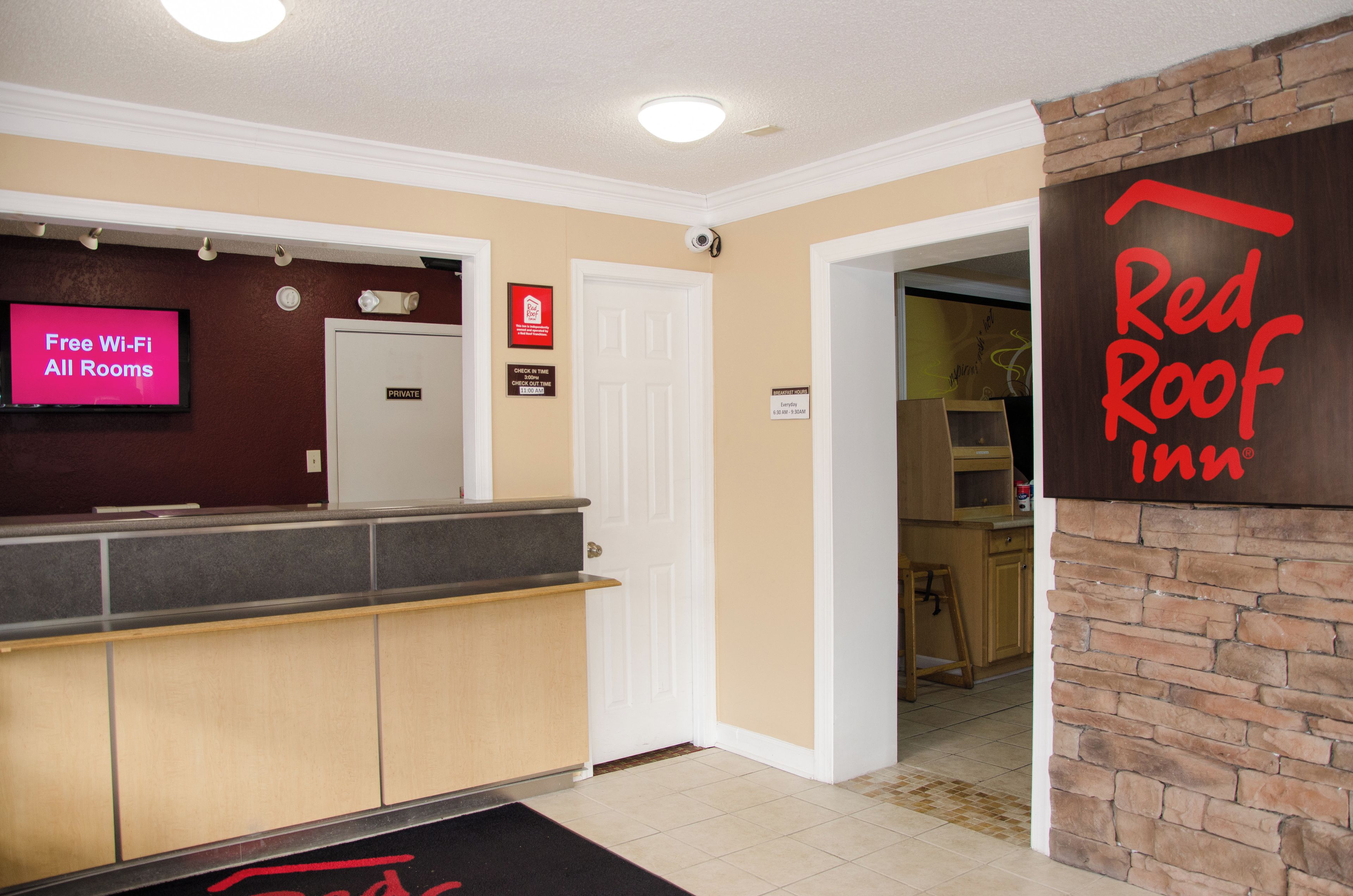 A hotel reception area with a Red Roof Inn sign, a digital display advertising free Wi-Fi, and a private room door.