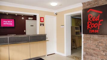 A hotel reception area with a Red Roof Inn sign, a digital display advertising free Wi-Fi, and a private room door.