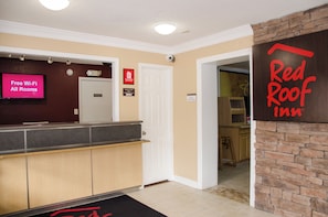 A hotel reception area with a Red Roof Inn sign, a digital display advertising free Wi-Fi, and a private room door. - Red Roof Inn Williamsburg (Williamsburg)