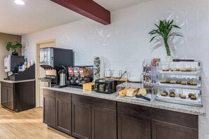 A hotel breakfast area with a coffee machine, toaster, and a display case with pastries. - Red Roof Inn Williamsburg (Williamsburg)