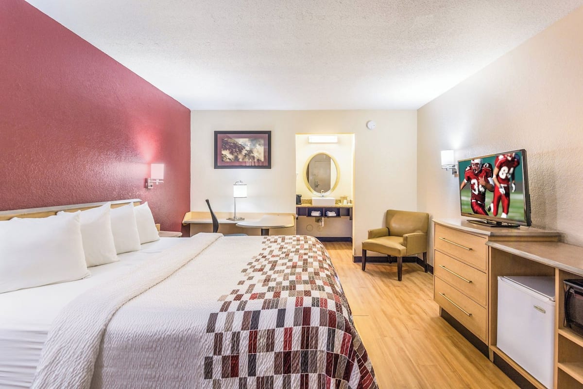 A hotel room with a bed, desk, chair, TV, and a small refrigerator.