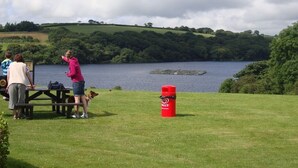A picnic area with a table and benches, a red cooler, and a lake with a dock in the background. - Llysyfran Farm B&B (Clarbeston Road)