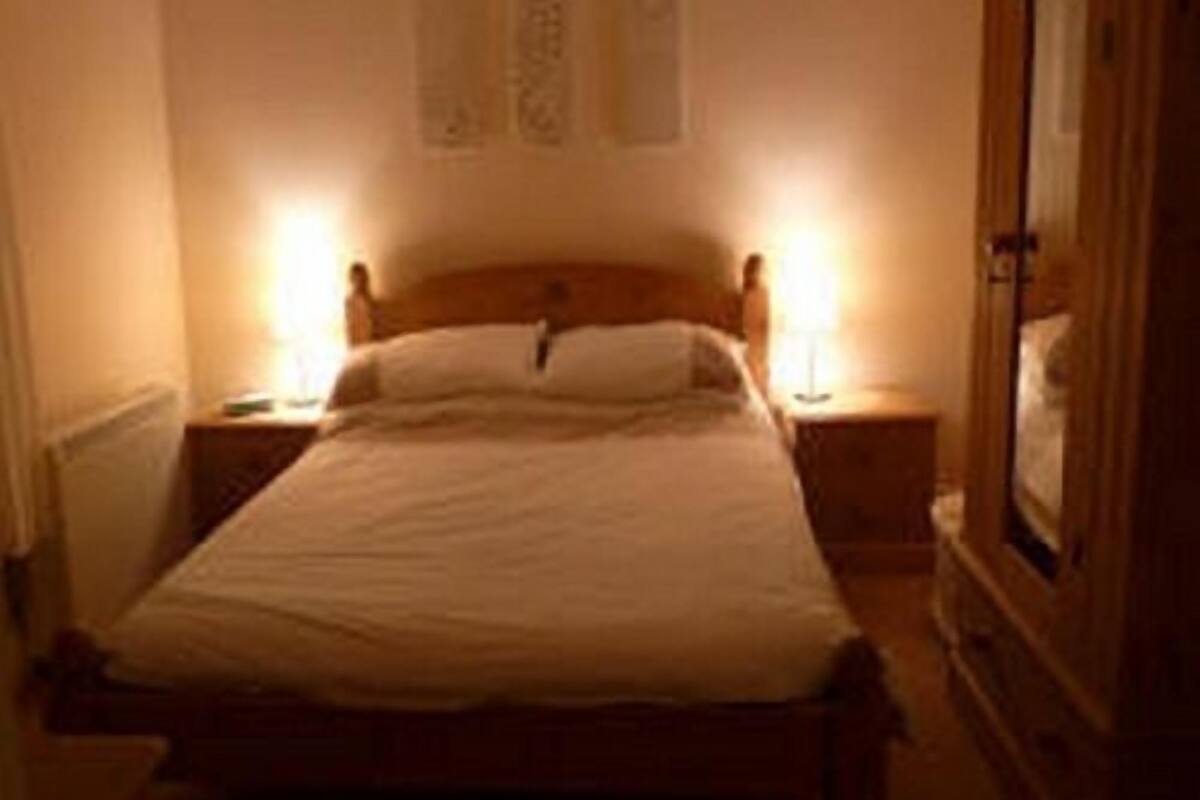 Une chambre à coucher faiblement éclairée, avec un lit en bois, deux tables de chevet et une petite table d’appoint.