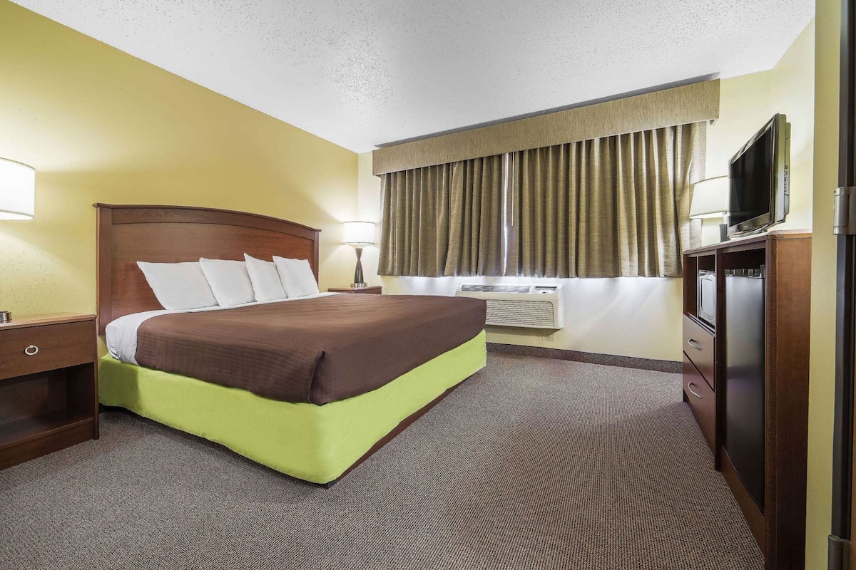 A hotel room with a bed, a desk, a television, and an air conditioning unit.