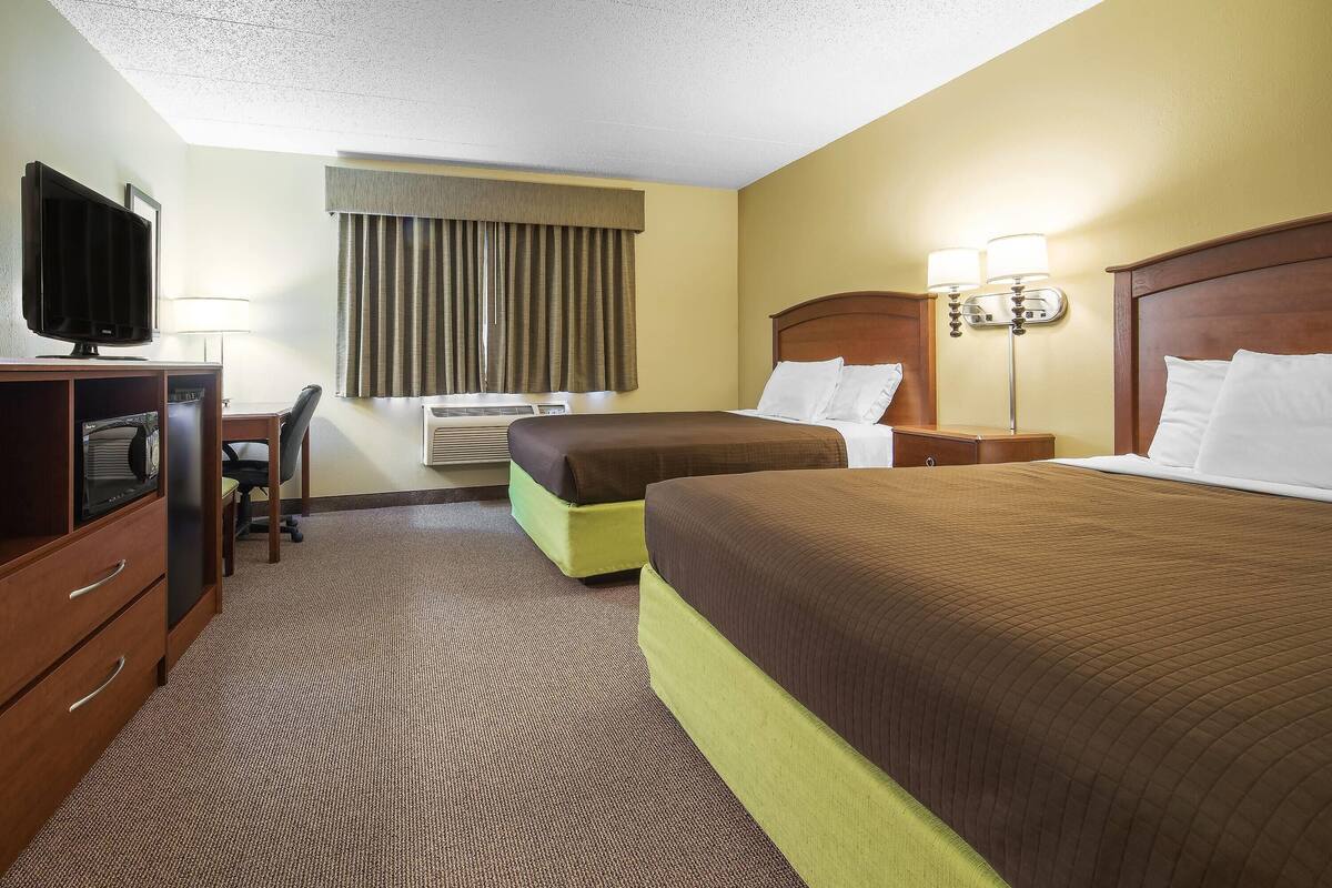 A hotel room with two beds, a desk with a television, a chair, and a window with curtains.