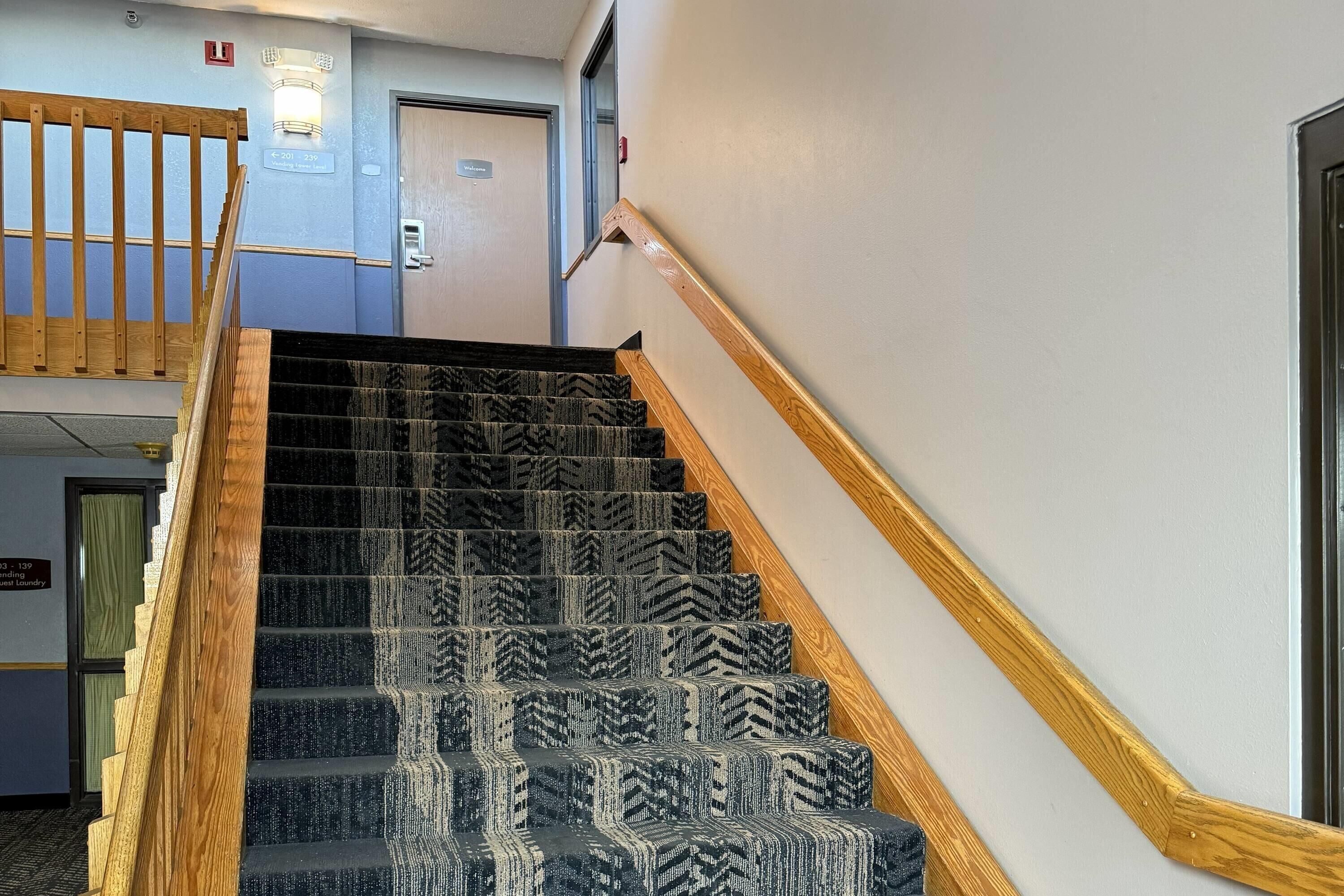 A staircase with patterned carpet and wooden handrails, leading to a room with a door and a sign above it.