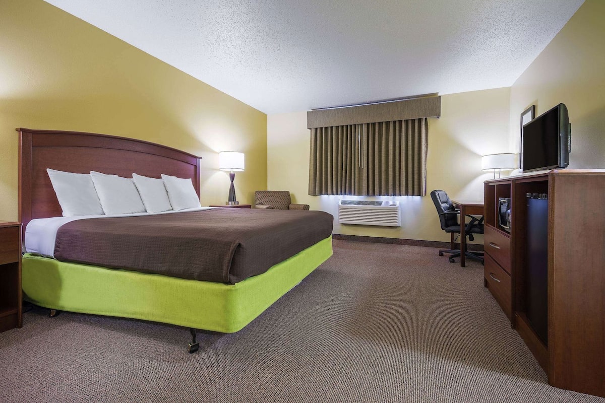 A hotel room with a bed, desk, chair, TV, and air conditioning unit.