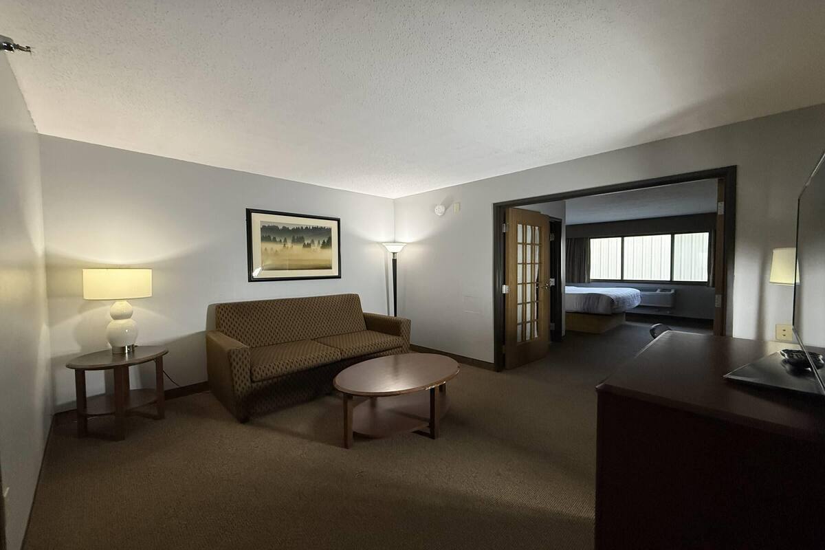 A hotel room with a sofa, a small table, a lamp, a bed, and a desk.