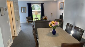 A dining area with a table set for four, a vase of flowers, and a view of the outdoors through a window. - The Taber Inne & Suites (Mystic)