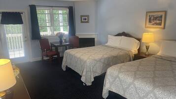 A hotel room with two beds, a desk, a chair, a fireplace, and a window with curtains.