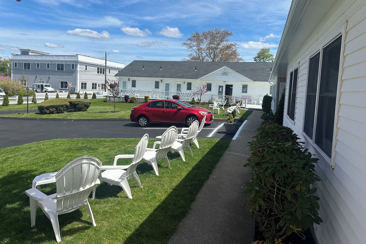 A red car parked in front of a white building with a lawn and outdoor seating area.