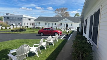 A red car parked in front of a white building with a lawn and outdoor seating area.