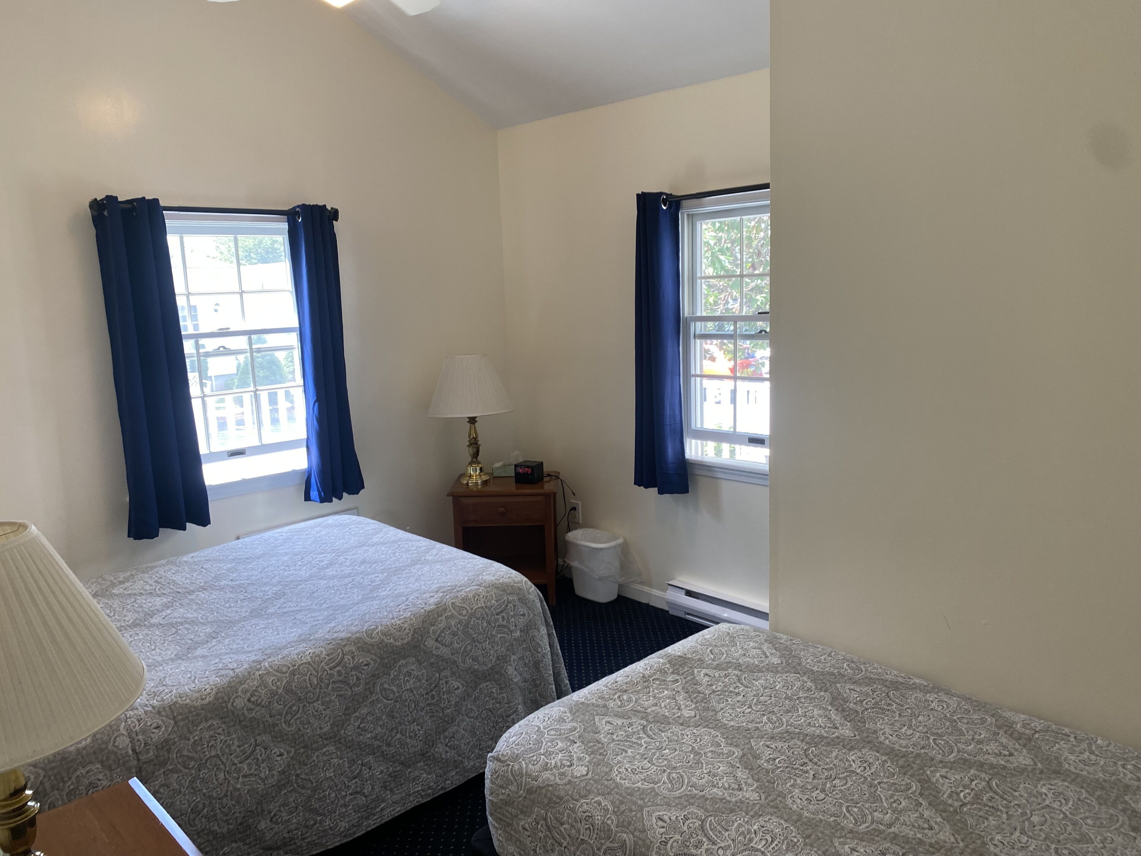 A hotel room with two beds, a nightstand with a lamp, a small table, and a window with curtains.