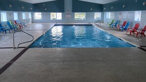 An indoor swimming pool with a tiled floor, safety signs, and colorful chairs around the pool. - The Taber Inne & Suites (Mystic)