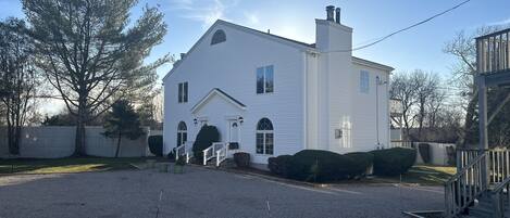 A white two-story house with a front porch, a chimney, and a gravel driveway.